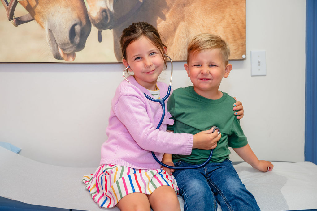 a young girl using a stethoscope on her brother
